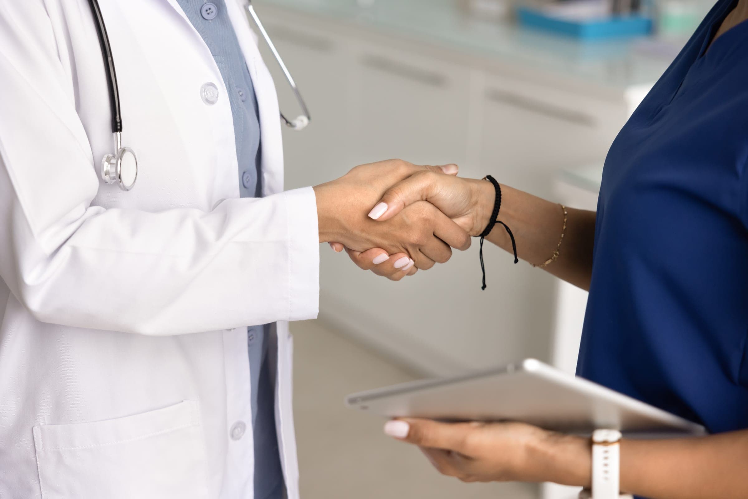 A physician in a white coat shaking hands with a colleague in scrubs, both cropped at the shoulders.